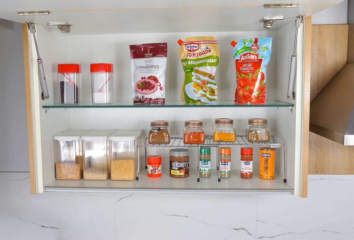 An expandable storage rack with spices, grains in boxes, and some condiments
