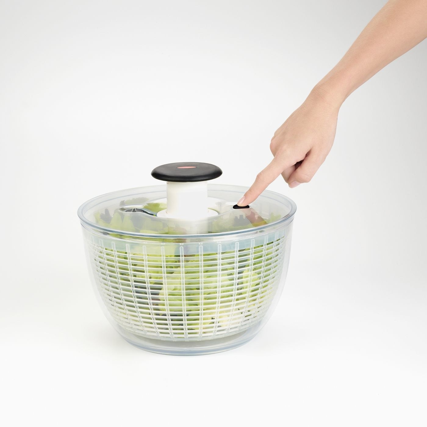 white salad spinner with lettuce inside and a model&#x27;s arm pressing the top knob