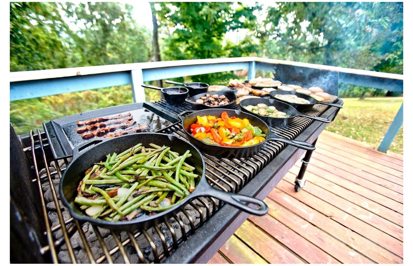 outdoor grill with several cast iron skillets cooking vegetables