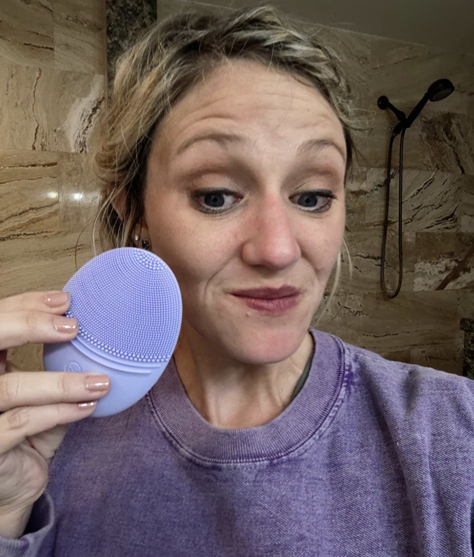 a person holding their purple silicone face cleansing brush