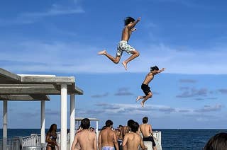 A group of kids jump off a dock while more kids watch