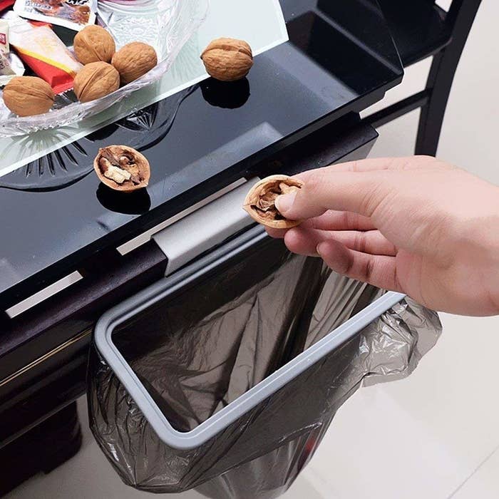 A person throwing walnut shells in the garbage bag attached to the holder.