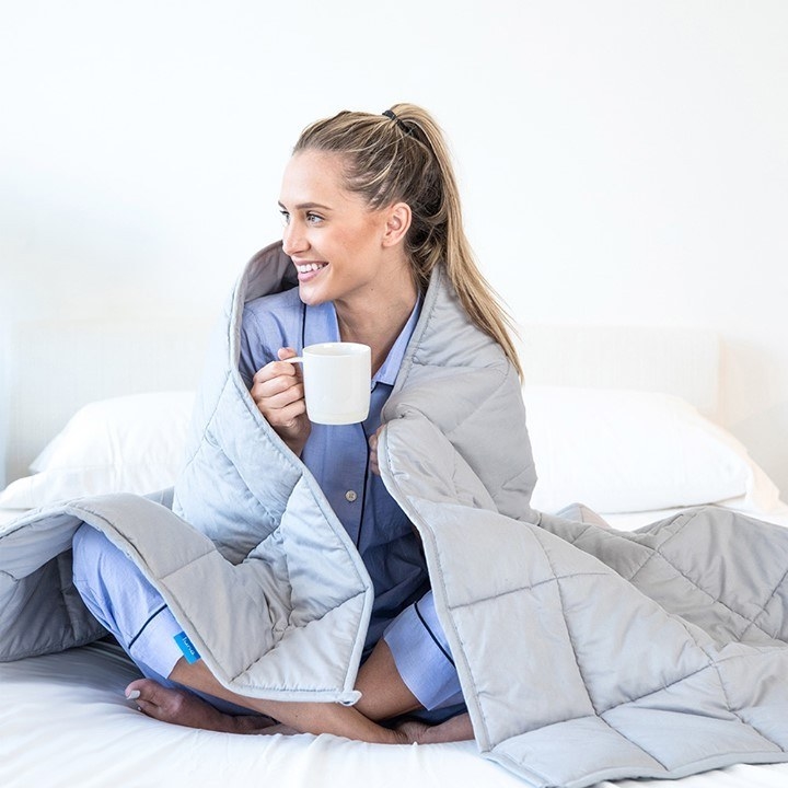 A smiling person wrapped in the blanket and sipping a hot beverage