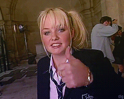 Baby Spice, dressed in a school uniform, gives a thumbs up to the camera
