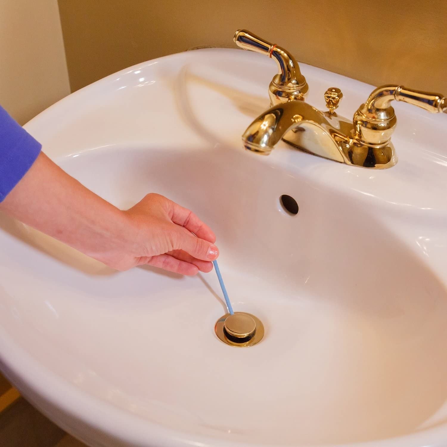 Someone inserting one of the deodorizing sticks into a sink drain