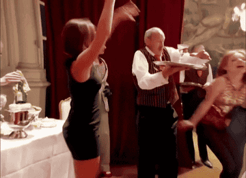 Posh Spice grabs a glass of champagne from a waiter and dances around