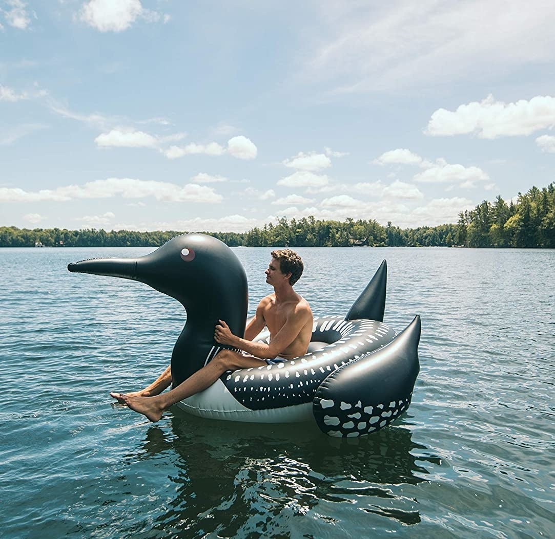 a person sitting on a loon-shaped float in a lake 