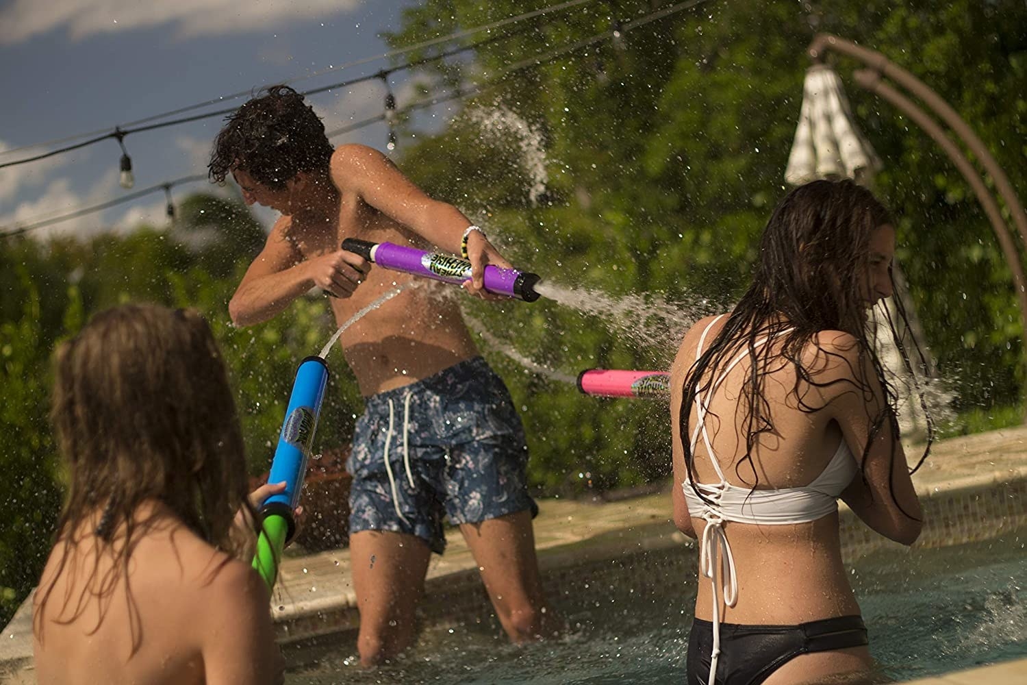 Three teenagers in a pool spraying each other with the water guns