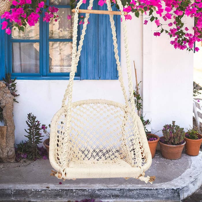 A macrame swing hanging outside a white house with blue windows.
