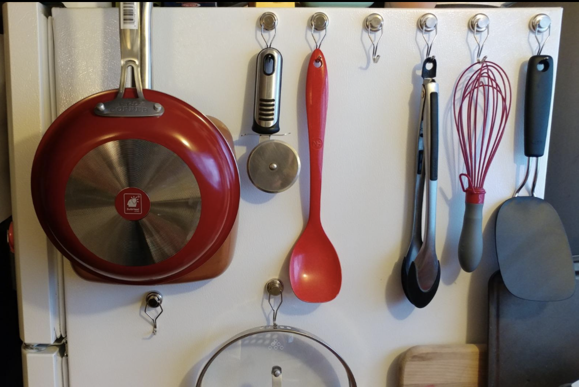 magnetic hooks being used to hang a pan, spoon, tongs, whisk, spatula, and pizza slicer