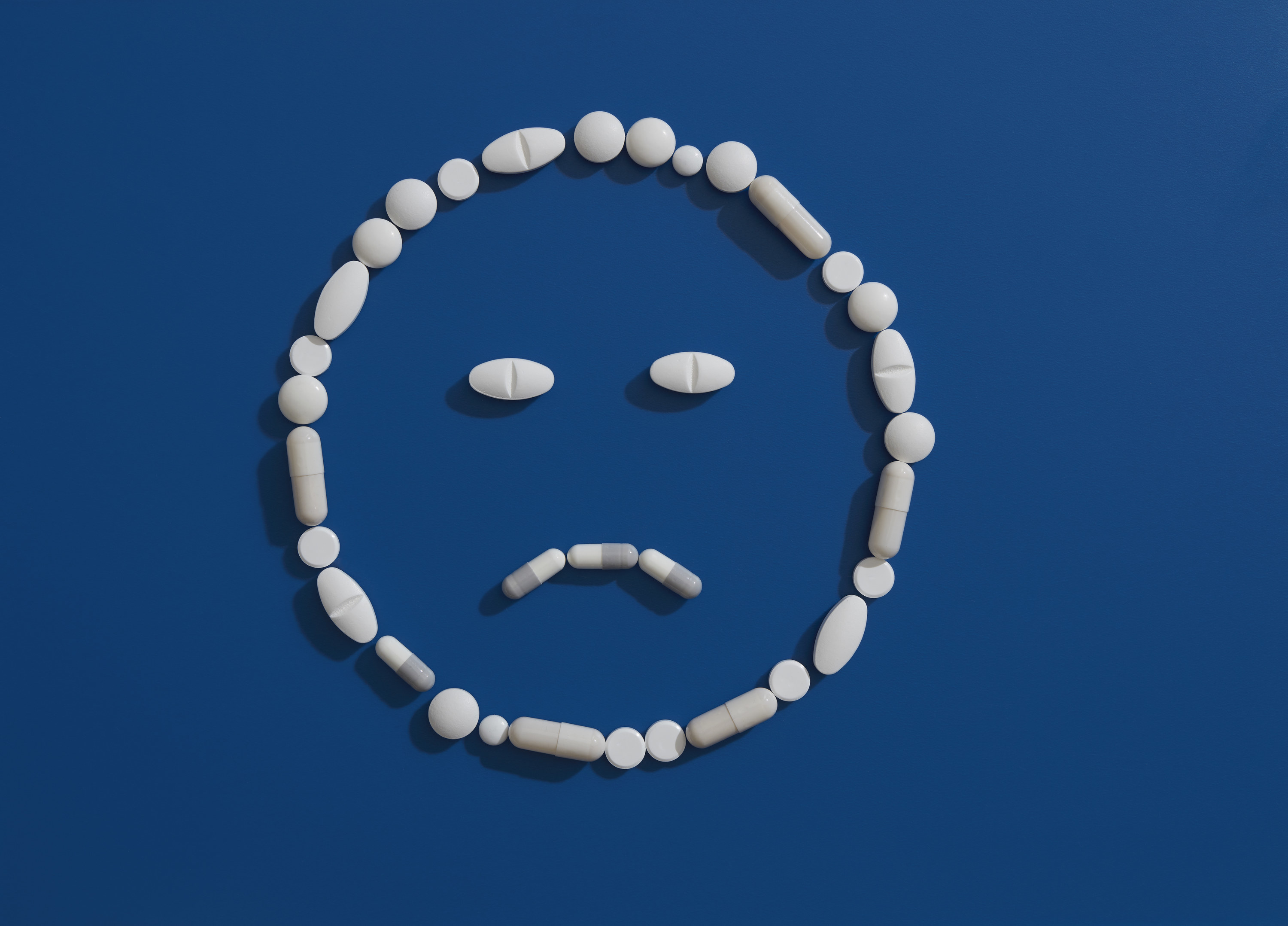 An image of pills on a blue background forming the shape of a sad face emoji