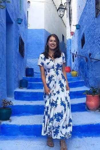 reviewer wearing the short-sleeved dress in white and blue while standing in a blue-painted alleyway