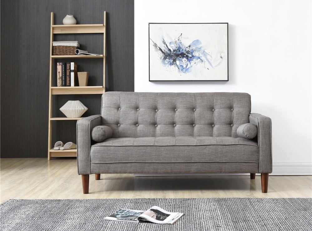 The gray sofa with a button-tufted back cushion and seat cushion, and wooden legs, in a living room