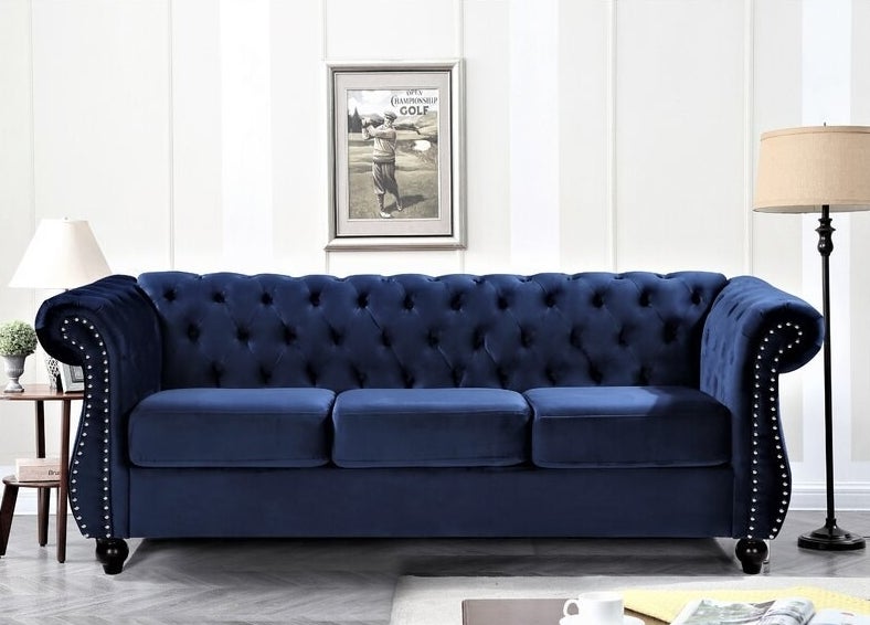 The blue velvet Chesterfield couch with button tufting on the back and sides as well as nailhead accents on both arms
