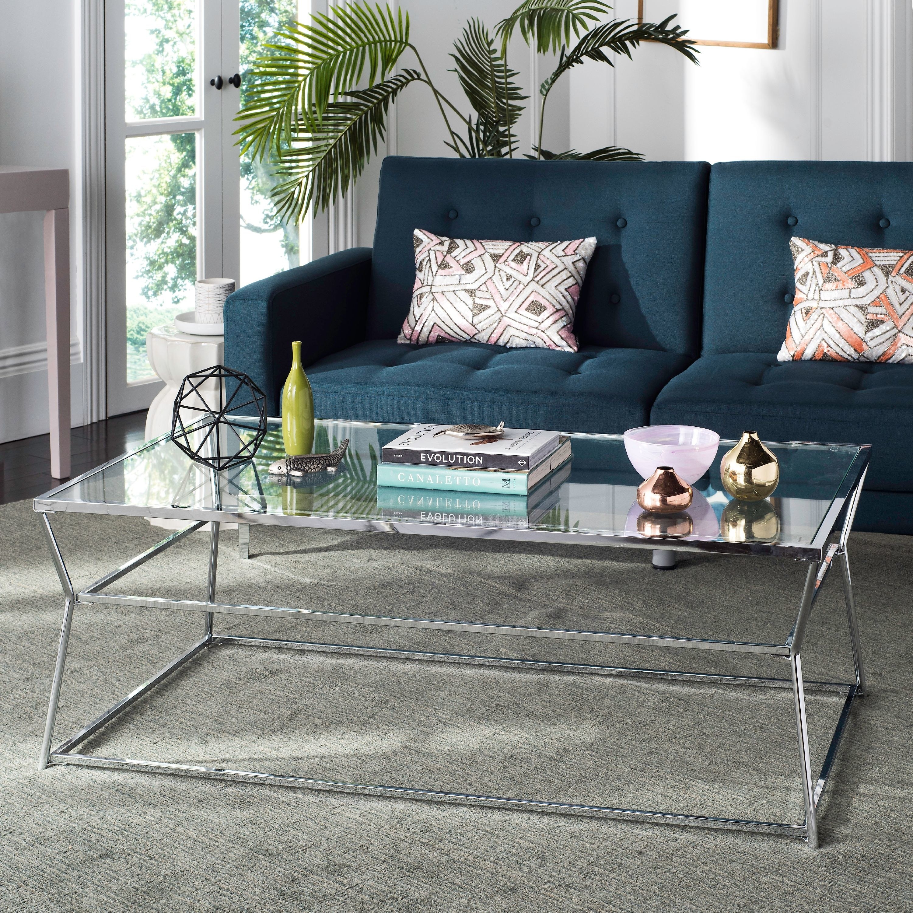 a glass coffee table on a grey rug next to a teal couch 