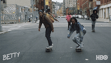 Two girls on skateboards do a kick flp in unison