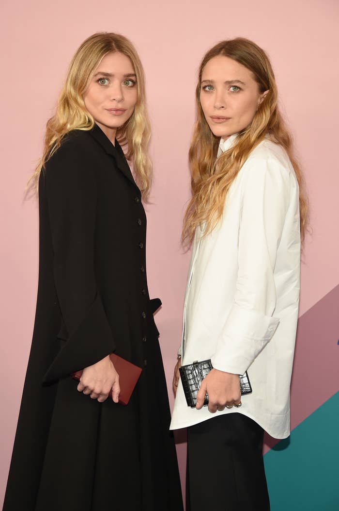 Ashley, in a long black coat, and Mary-Kate, in a white blazer and black pants, stand next to each other at the CFDA Fashion Awards in 2017