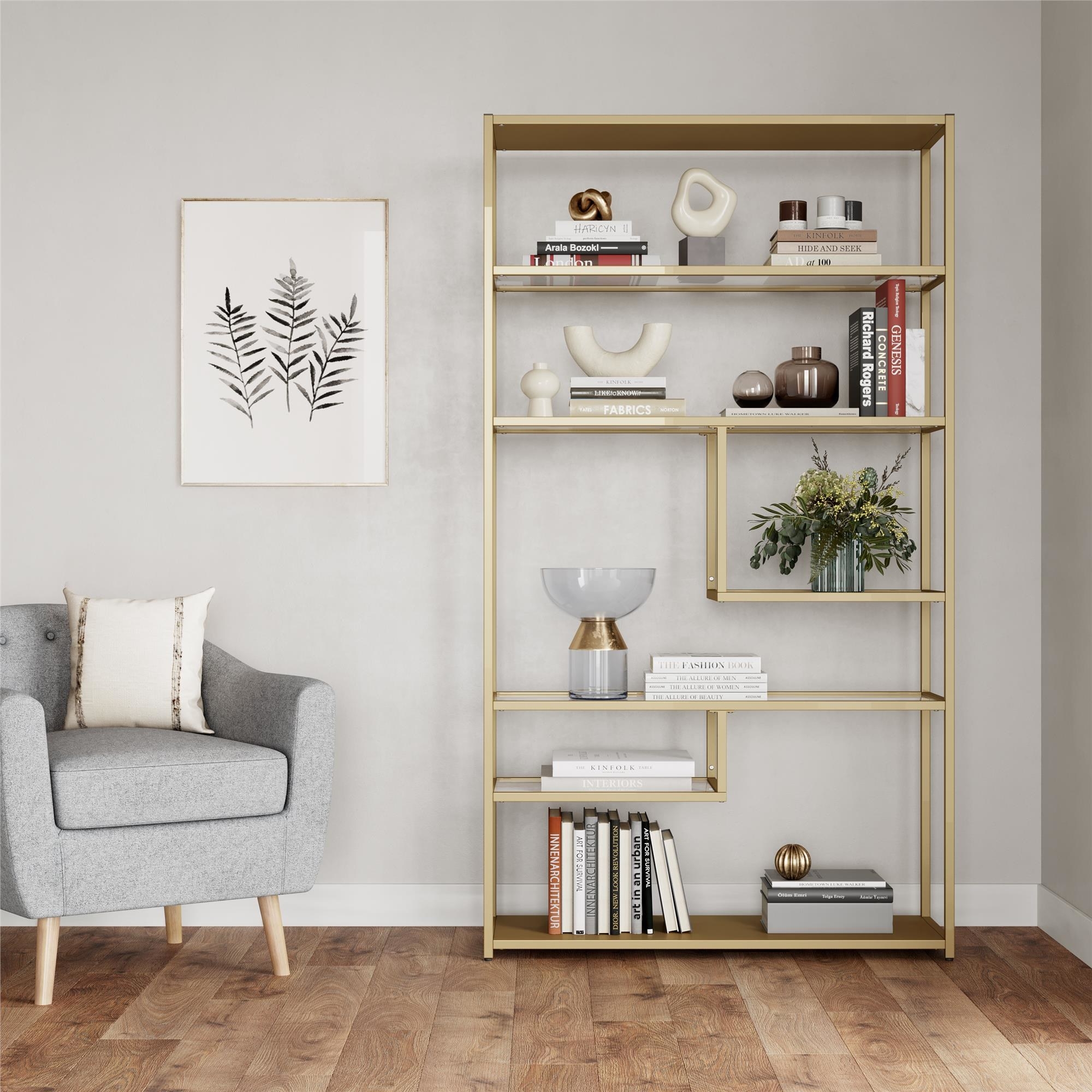 gold geometric book shelf with books and trinkets on it, next to a grey chair