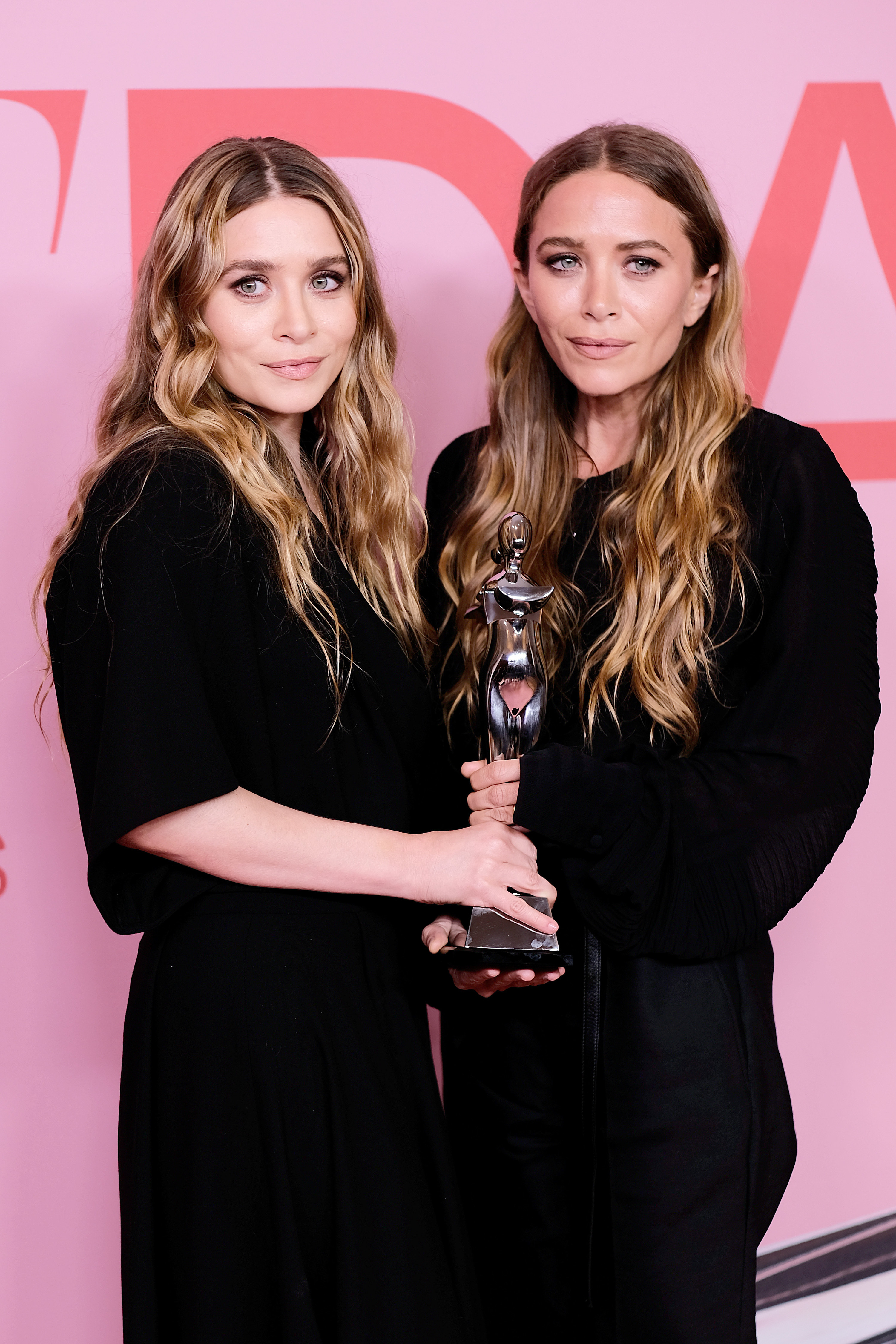 Ashley and Mary-Kate, both dressed in all black, holding their Accessory Designer of the Year Award together in 2019