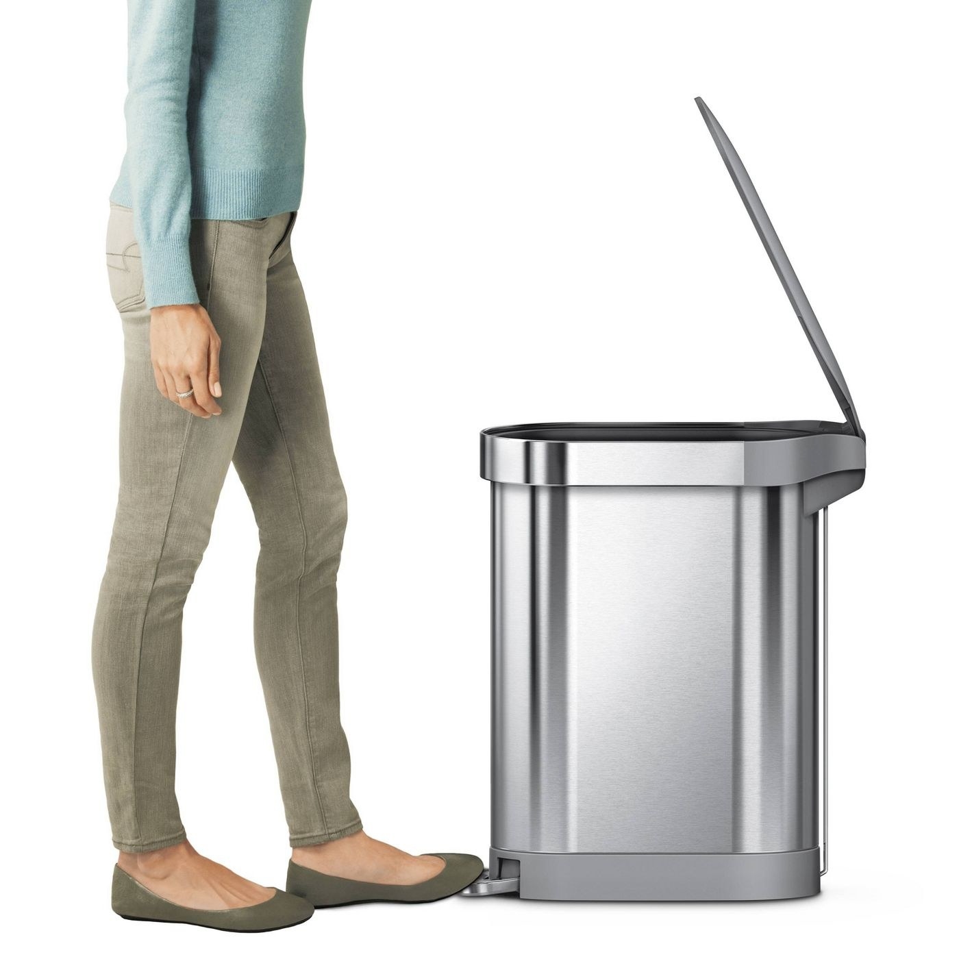 model stepping on the pedal of a stainless steel trash can with lid open