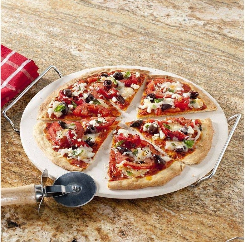 pizza stone and rack with pizza on top and a pizza cutter nearby