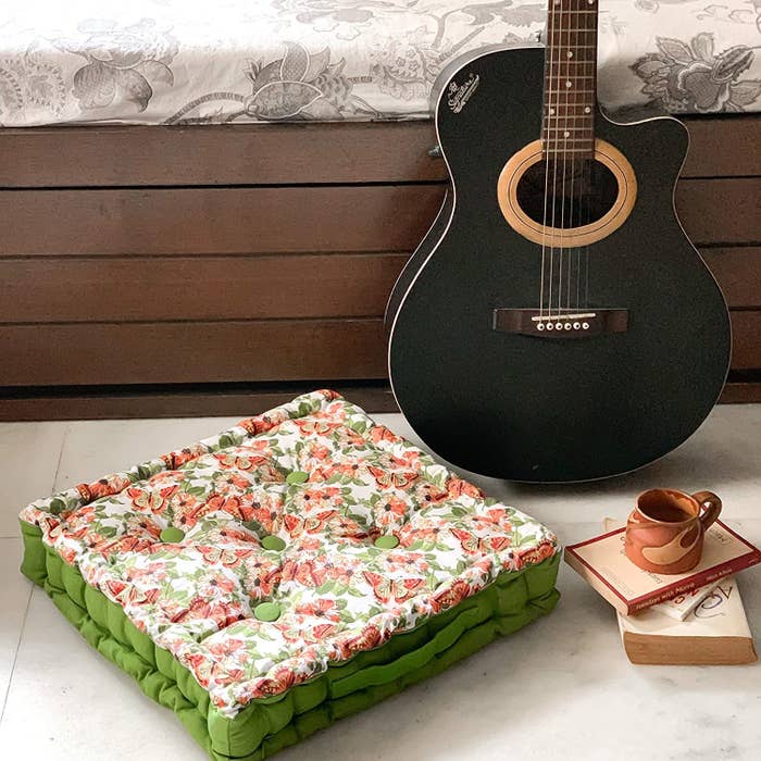A green and pink floor pillow with books and a guitar beside it 
