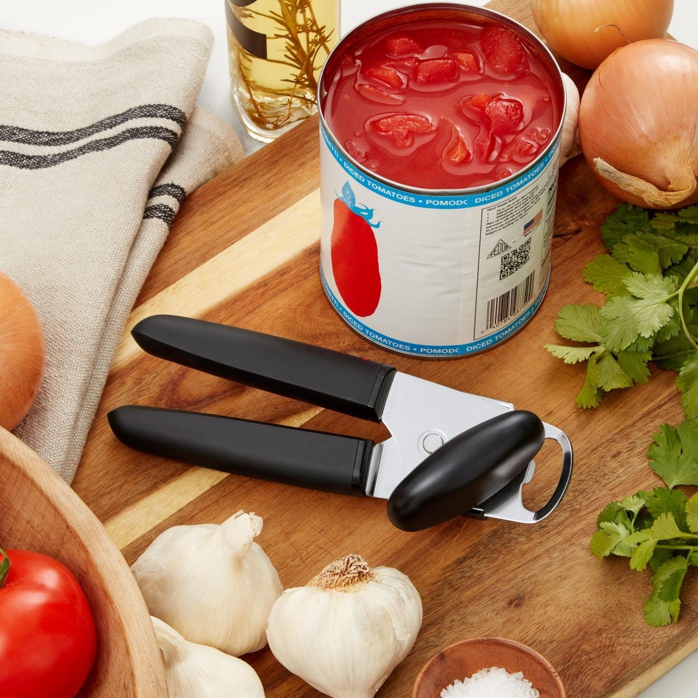 stainless steel can opener with black handles next to an open can of tomatoes