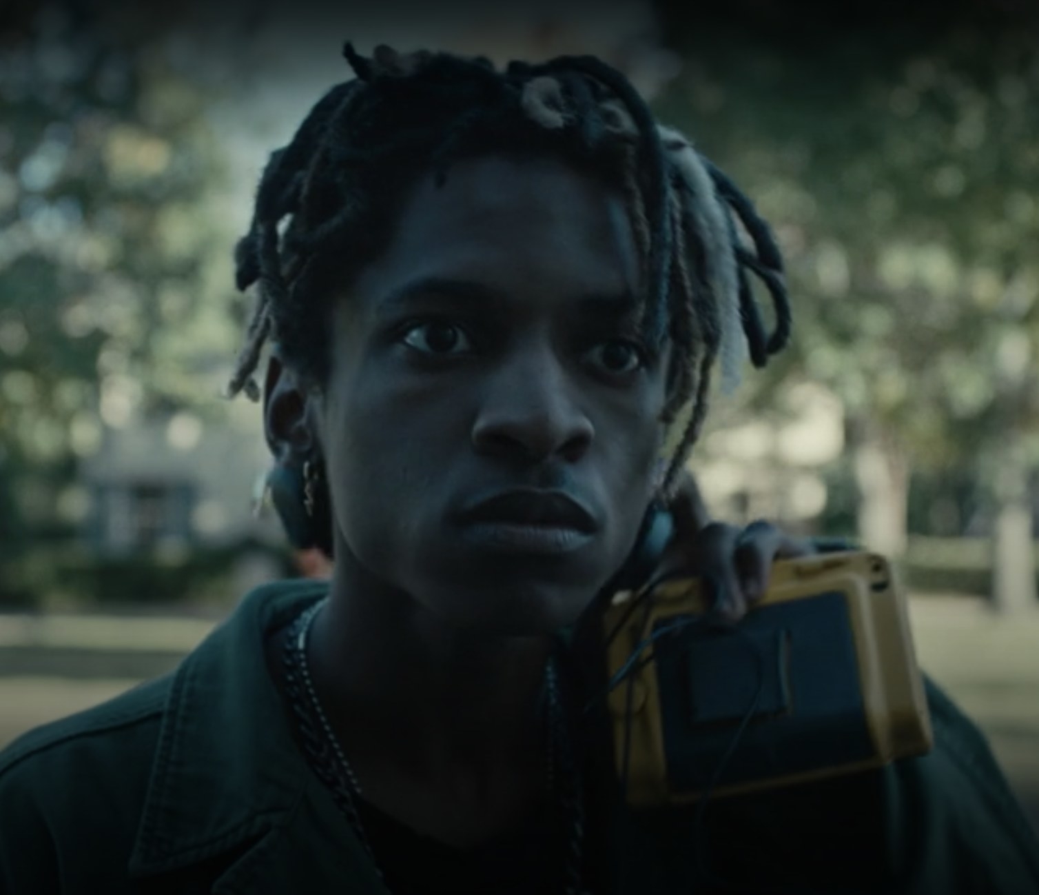 A teenager with short dreads wearing headphones and holding a yellow cassette walkman.