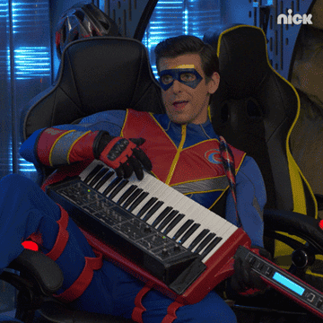 Man in superhero costume smugly plays a keyboard sitting on his lap.
