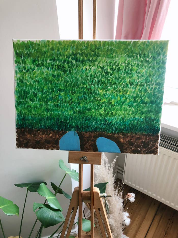 Painting of feet touching grassy area sitting on top of an easel in author&#x27;s room.