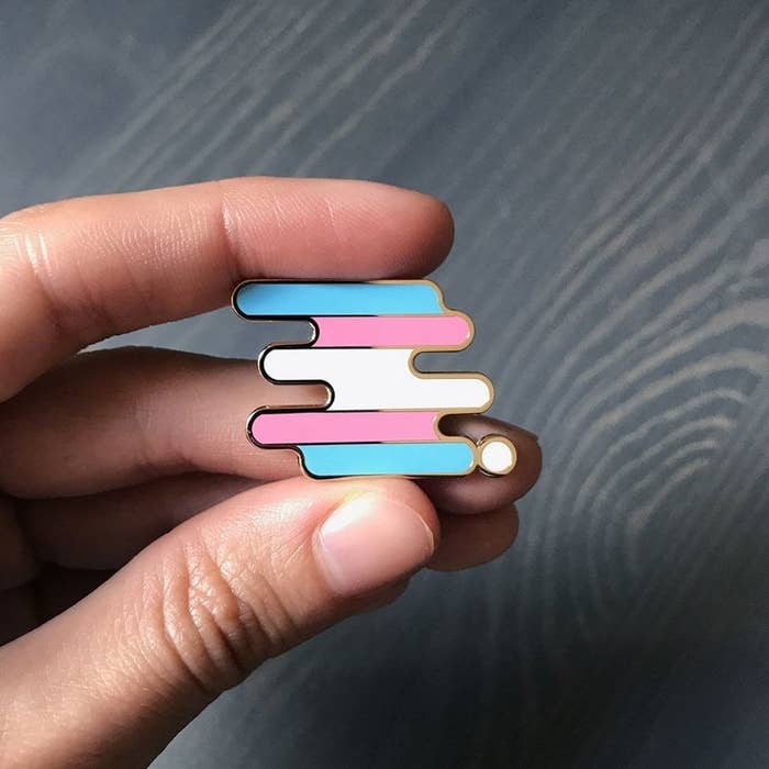 a hand holding the trans pride pin