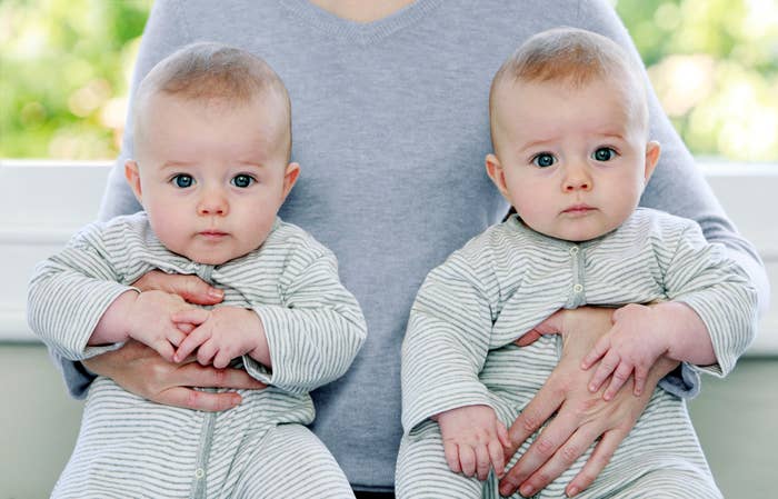 Two twin babies wearing matching stripey PJs being held on someone's lap