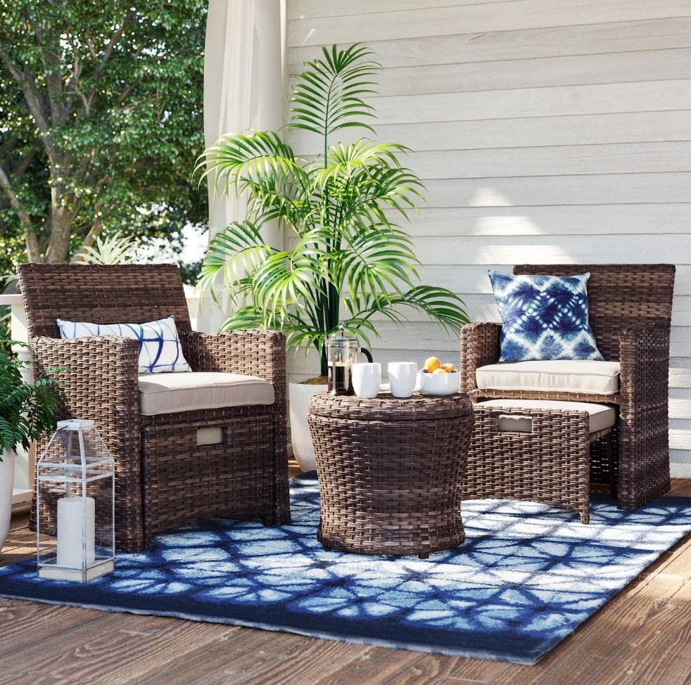 Brown wicker bistro set with two cushioned chairs, blue throw pillows, and round table 