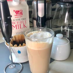 A customer review photo of the Zulay Original Milk Frother next to a frothy cup of coffee.
