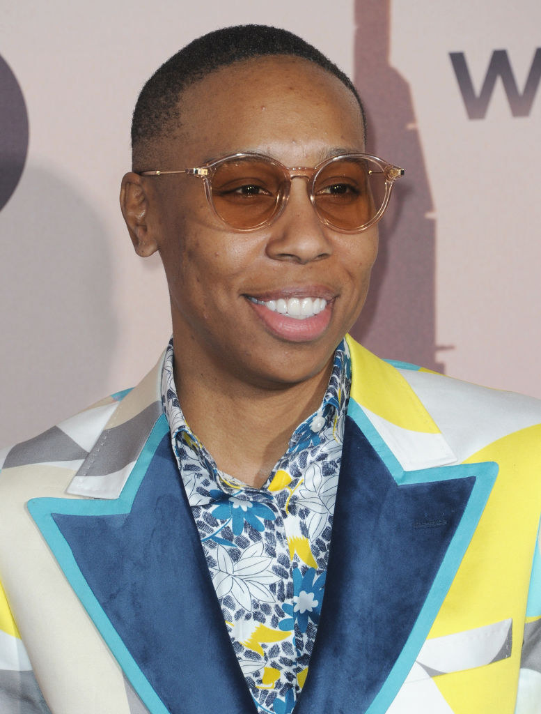 Waithe in a blazer with wide, colorful lapels over a colorful floral patterned shirt, wearing light sunglasses, smiling outside an event