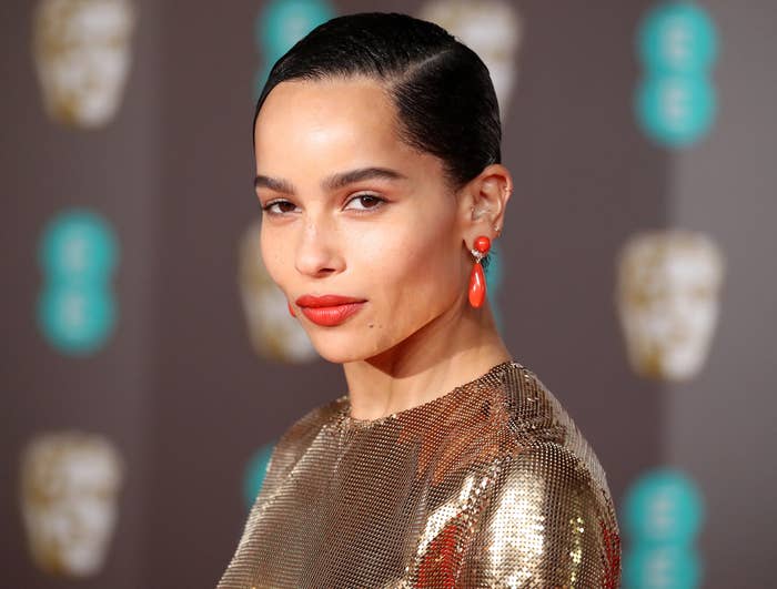 Zoe looks toward the camera in a gold shimmering dress at an event