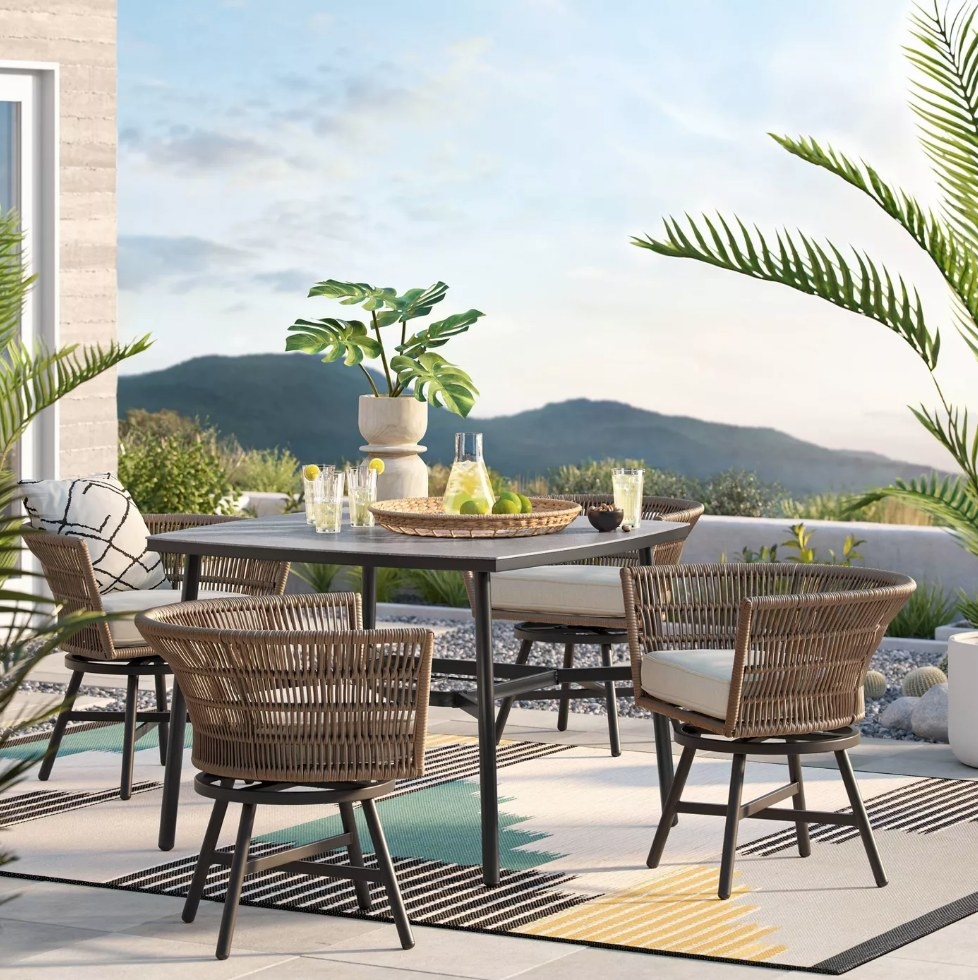 Square outdoor dining table surrounded by wicker swivel chairs 
