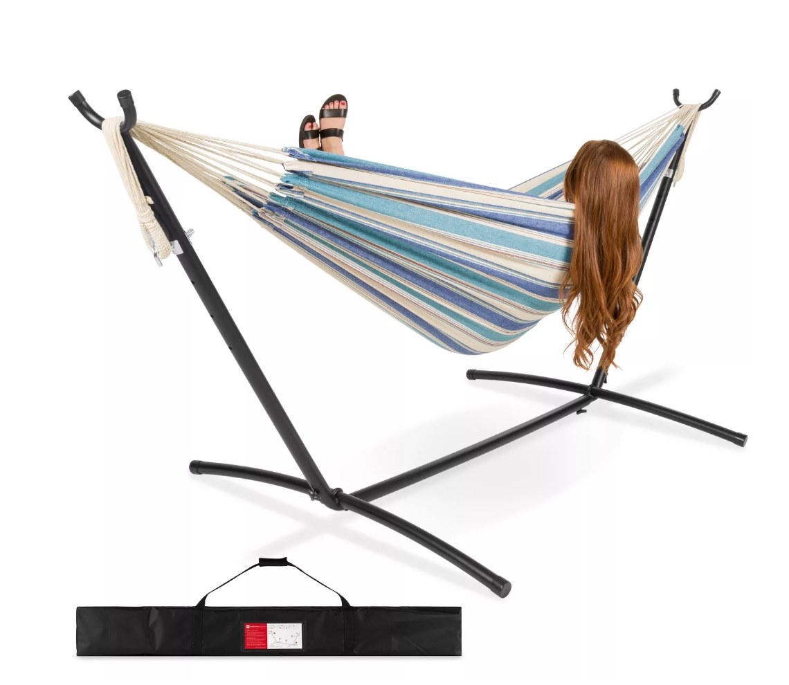 Model lounging in blue striped hammock on black hammock stand 