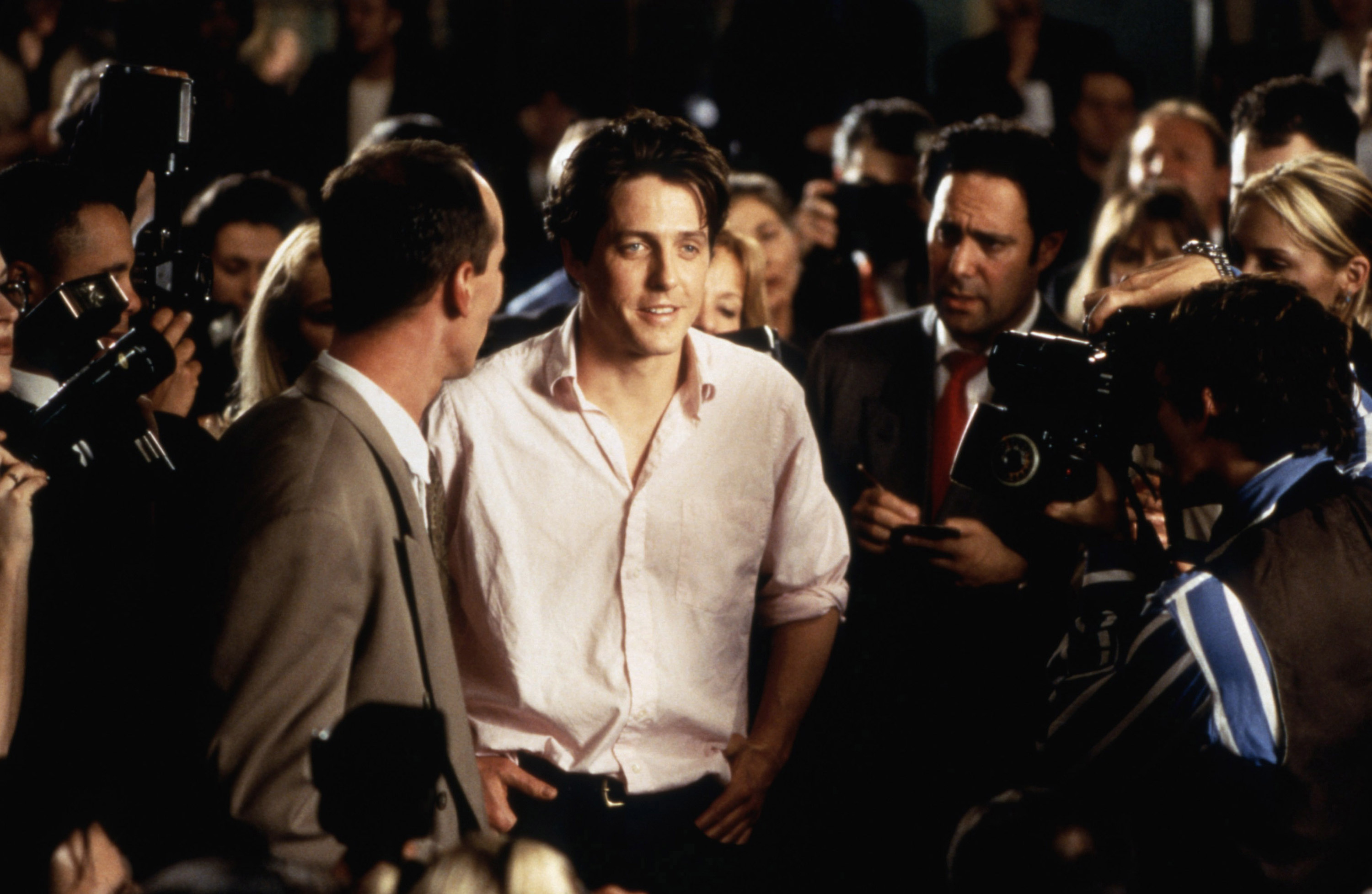 Hugh smiles while surrounded by reporters in a scene from Notting Hill