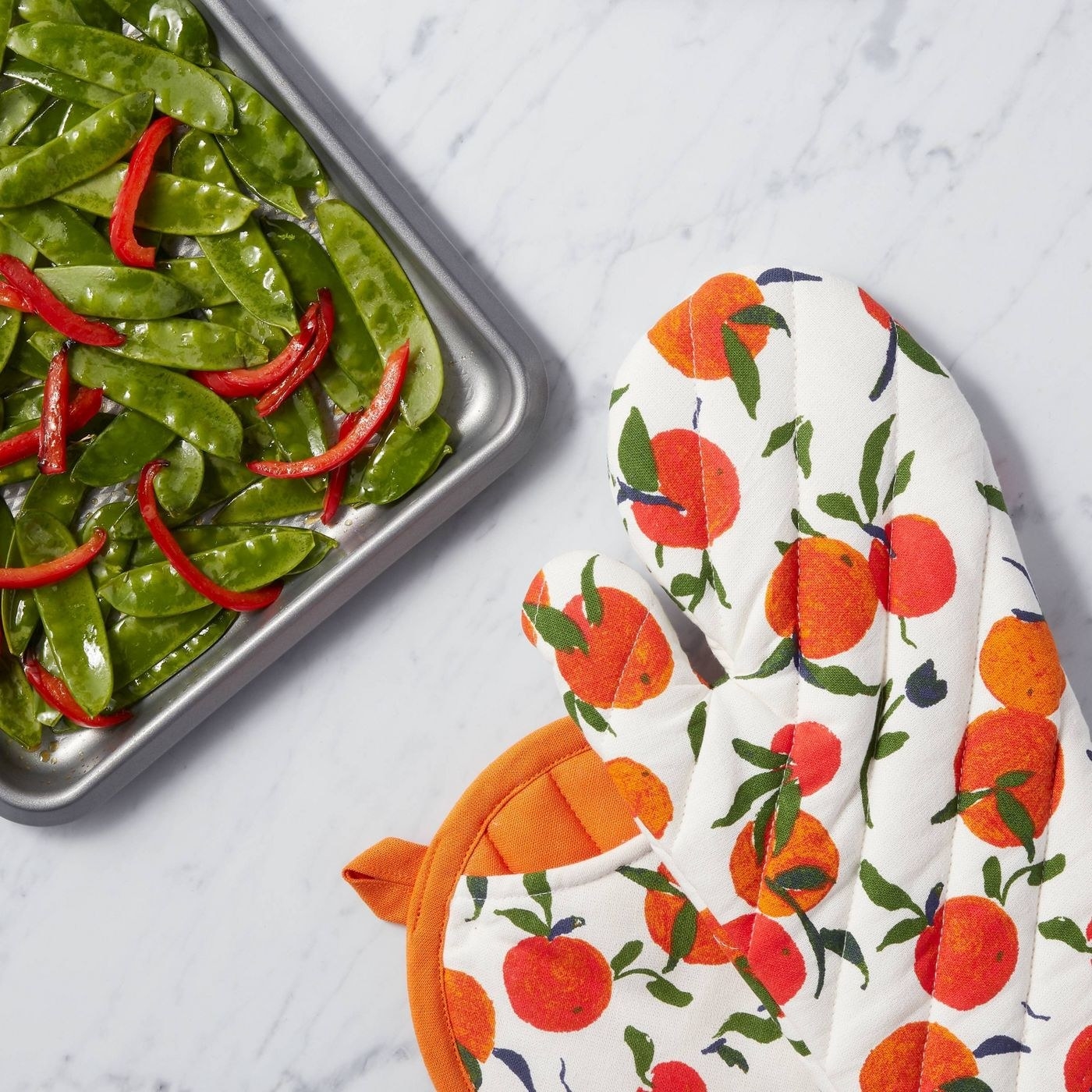 the orange patterned mitt and potholder next to a sheet pan of vegetables