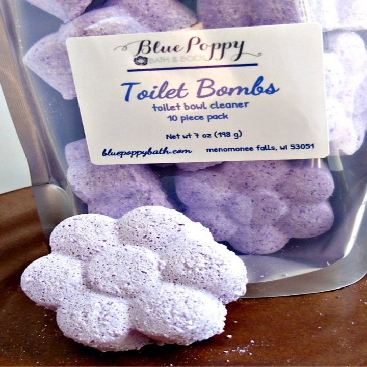 a bag of toilet bombs sitting next to a light purple, flower-shaped toilet bomb 
