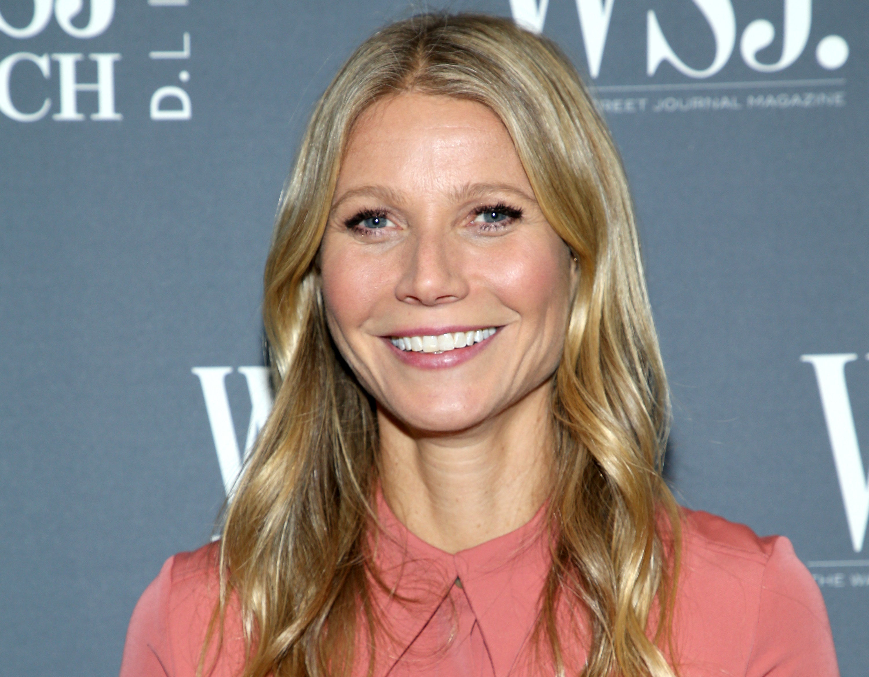 Gwyneth smiles in a pink shirt at an event