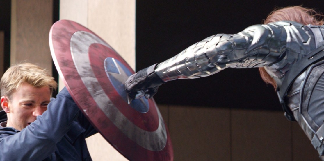 Captain America holds up his shield to block a punch from the metal arm of the Winter Solider.