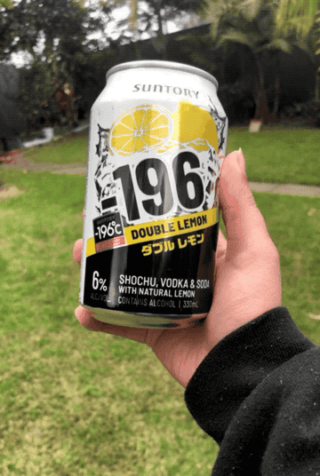 A hand holding a can of Minus 196 Double Lemon before bringing it and obscuring the camera