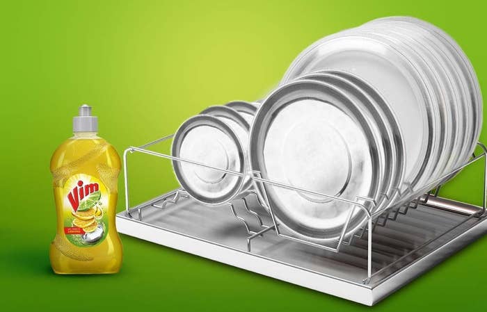 A bottle of Vim dishwashing liquid next to some clean plates on a dish rack.