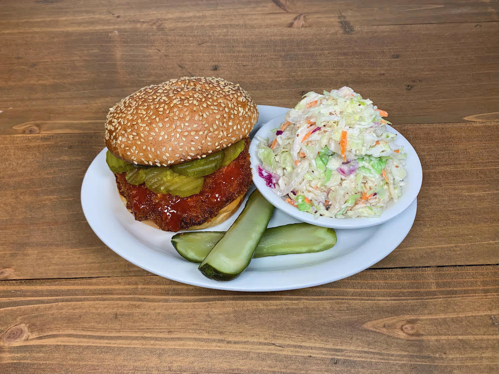 Chicken schnitzel sandwich with pickle spears and coleslaw