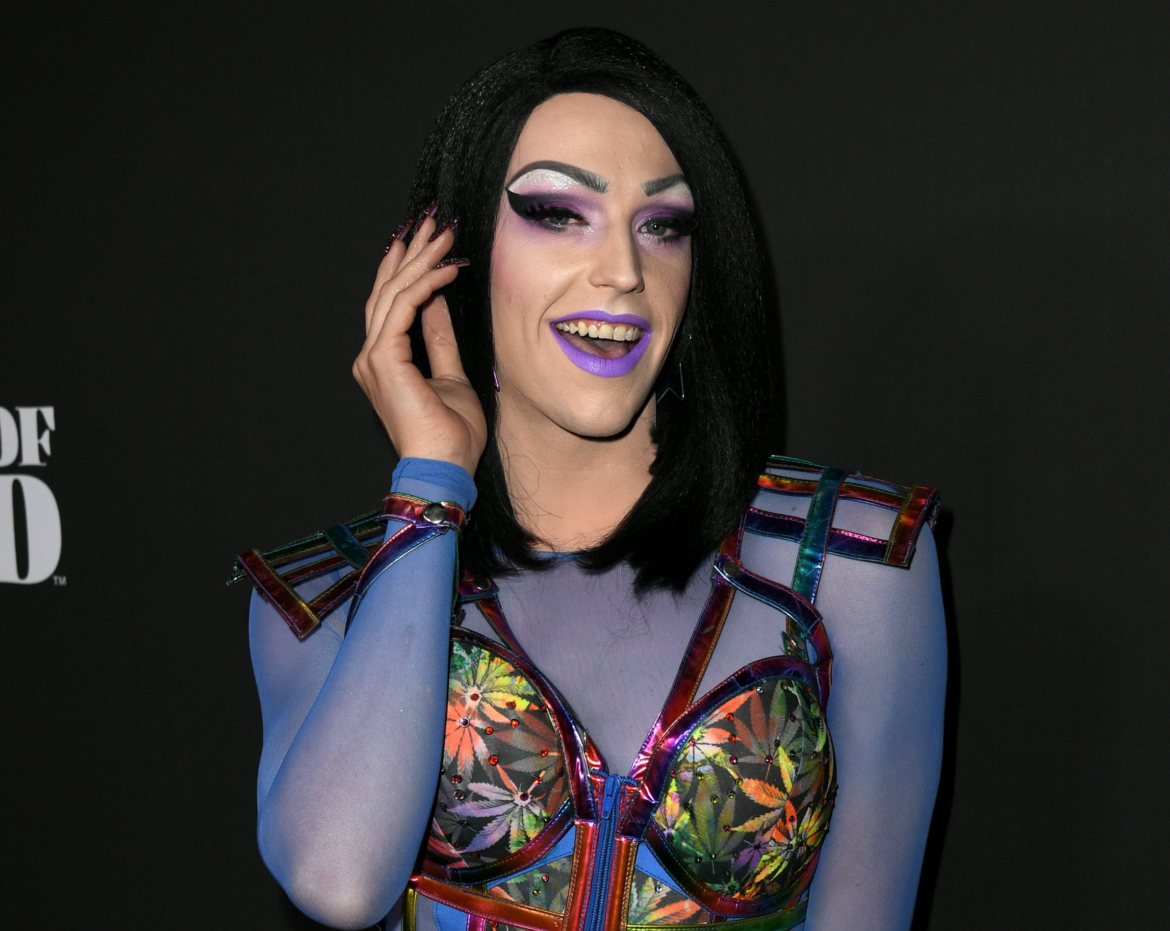 Laganja smiles while wearing a short black wig and purple makeup