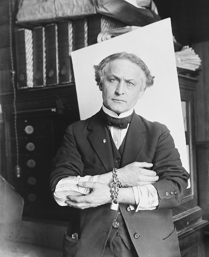 An older looking Harry Houdini posing with chains on his wrists