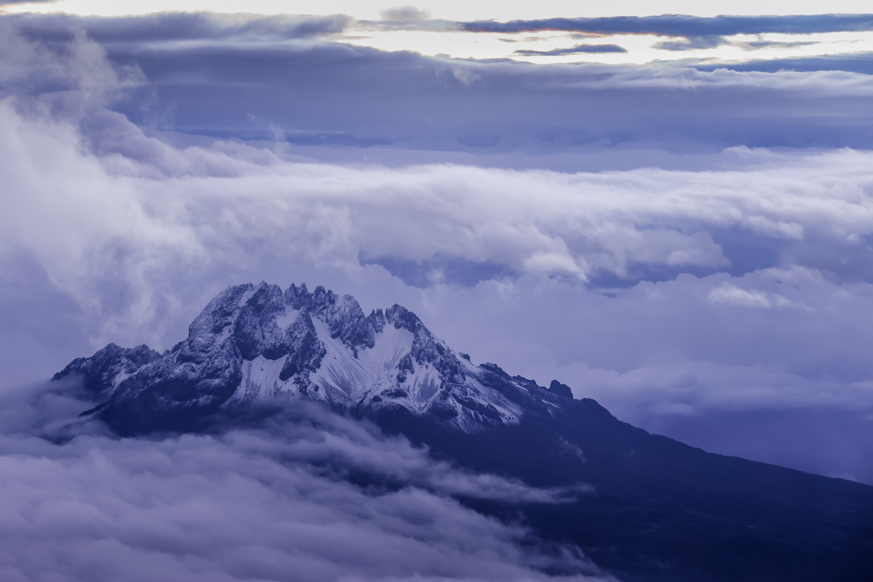 View of snow-capped Mount Kiliminjaro with white clouds surrounding the peak.