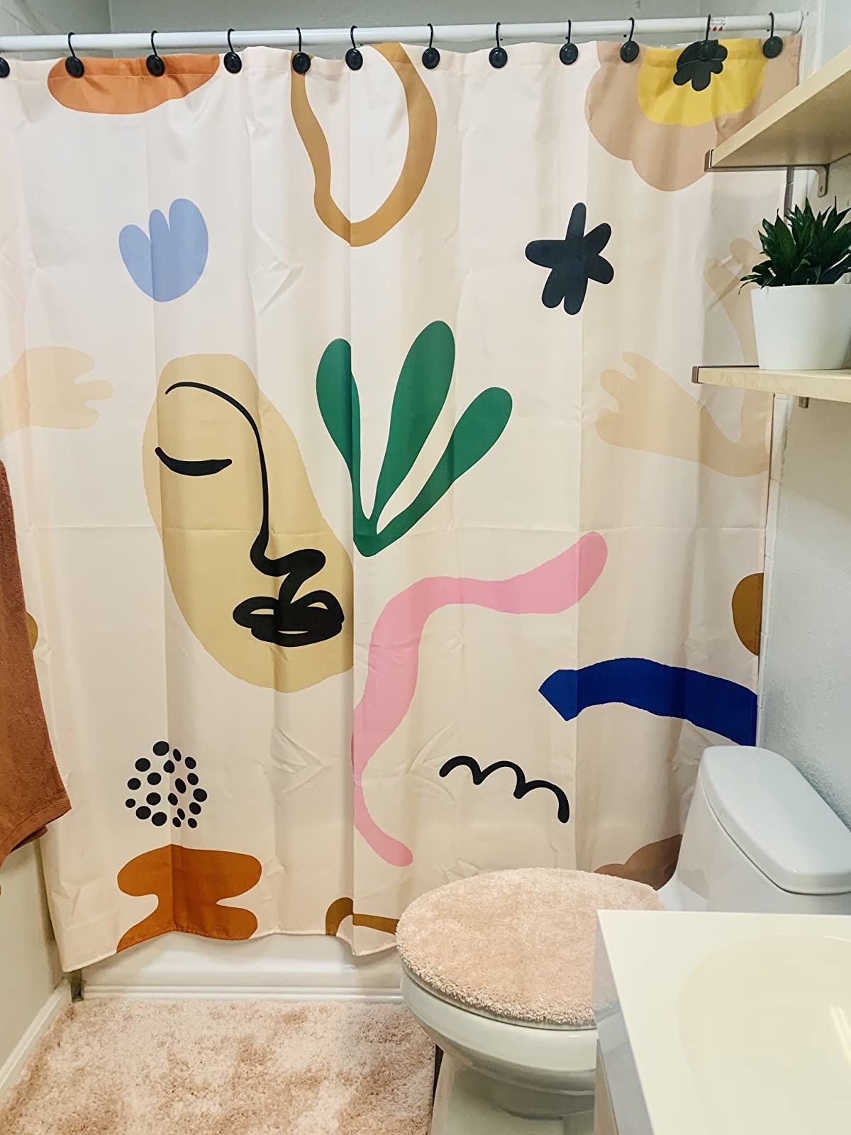 a reviewer photo of the abstract shower curtain that has fun shapes and squiggles in different colors and an abstract drawing of a face